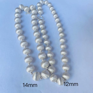 Détail montrant les colliers de perles argentées de 12mm et 14mm avec fini mat brossé