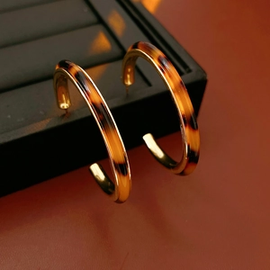 Detailed close-up of C-shaped resin earrings with golden metal base and amber tortoise pattern