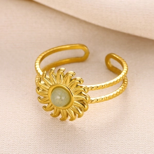Macro detail of gold sunflower ring featuring a round green gemstone on beige fabric