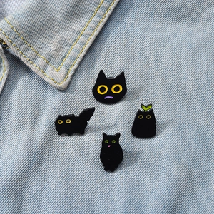 Detailed view of four black cat enamel pins styled on a denim jacket collar