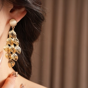 Close-up of golden leaf tassel earrings with cat eye stones worn by a model