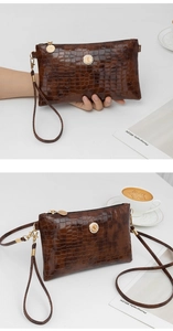 Detail of brown crocodile pattern clutch bag with gold hardware and wrist strap