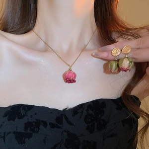 Close-up of elegant gold necklace and earrings set featuring real dried rose buds