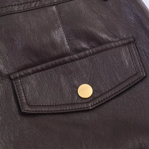 Detalle de los pantalones de cuero sintético marrón oscuro con botón de metal dorado