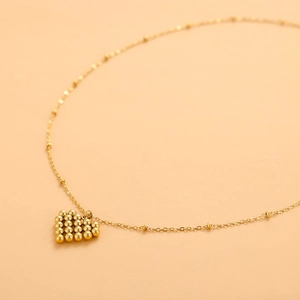Detail of a polished gold heart pendant crafted with tiny beads on a satellite chain necklace