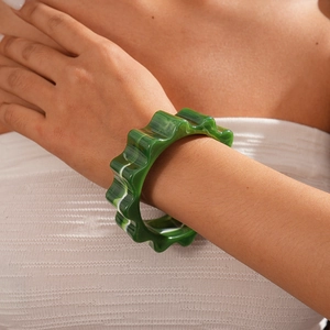 Close-up of a green marbled acrylic bangle with unique wavy gear edges on a model's wrist