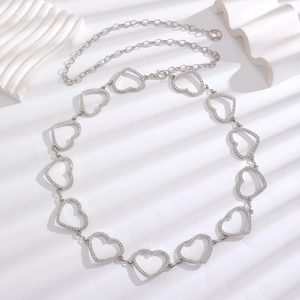 Detail of silver heart-shaped metal waist chain with rhinestones on white wavy background