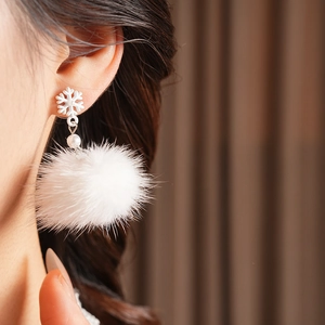 Detail of snowflake earring with fuzzy white pompom and pearl on model's ear