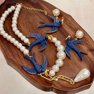 Macro view of vintage style bird necklace and pearl earrings on dark wood tray