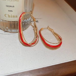 Detail of geometric red enamel and gold hoop earrings on a minimalist white texture