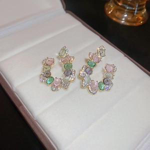 Macro shot of colorful zircon stones set in gold C-shaped earrings on white velvet