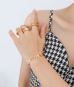 Dettaglio di un bracciale dorato a maglie quadrate e anelli minimalisti su un polso