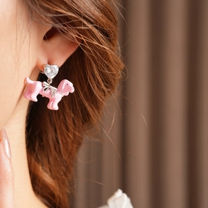Close-up of a pink puppy earring with a silver bow and heart gemstone on a model
