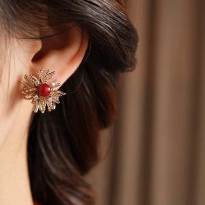 Macro detail of firework shape gold earring with red stone and zircon on ear