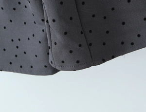 Detailed macro view of dark grey fabric with black flocked polka dots and neat hem stitching