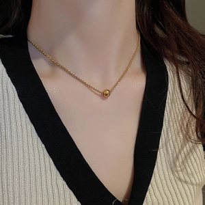 Detailed view of a gold bead pendant on a fine chain worn by a model in casual attire