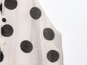 Close-up detail of cream polka dot fabric texture with black buttons on summer camisole set