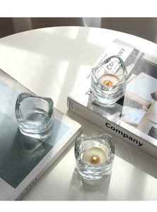 Close-up of three wavy glass candle holders with lit tea candles on a minimalist desk