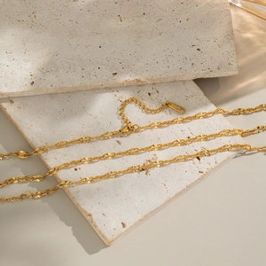 Detail of gold chain necklace with textured disc links on beige travertine stone