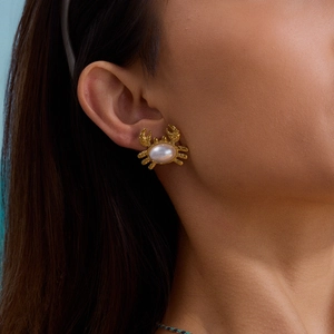 Dettaglio di un orecchino a forma di granchio in oro con perla su una modella