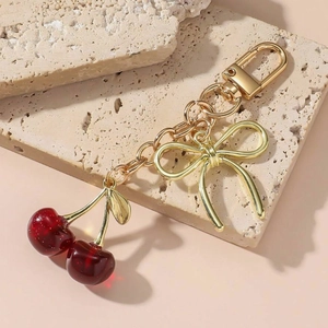 Shiny red cherry pendant keychain with golden bow on a decorative stone base