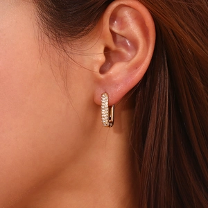 Close-up of a gold-plated rectangular earring with inlaid zircons worn by a female model