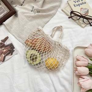 Detail of beige woven mesh bag filled with fresh fruits and bread on soft textured cloth