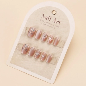Detail of nude pink press-on nails with cute cat motifs, bows and shiny rhinestones
