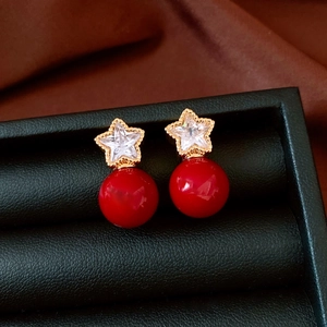 Detail of star-shaped earrings with white zircon and red pearl on black jewelry box
