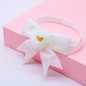 Close-up of white velvet pet bow tie featuring a soft faux fur pom and gold metal charm detail