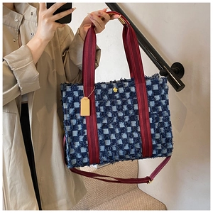 Detail of checkered denim tote bag with red strap and golden flower charm