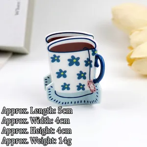 Detail view of coffee cup hair claw clip with blue floral patterns and tea bag charm