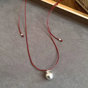 Close-up of matte silver apple pendant on a red cord necklace with detailed knotting