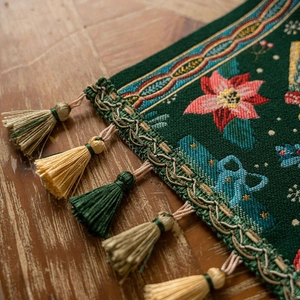 Green Christmas table runner with poinsettia embroidery and fringed edges on wood table
