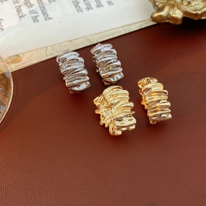 Macro shot of irregular textured gold and silver hoop earrings on brown leather surface