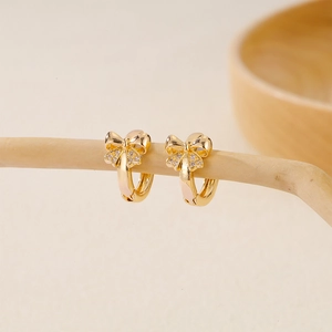 Gold plated bow knot hoop earrings with micro-set zircons on a rustic wood branch