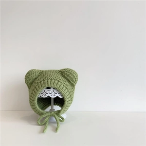 Detail of green knitted baby hat with bear ears and adjustable straps on a white stand