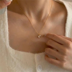 Close-up of a delicate gold chain necklace featuring drop and round zircon pendants on neck