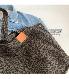 Detail of leopard print canvas tote bag featuring orange leather patch and metal snap button