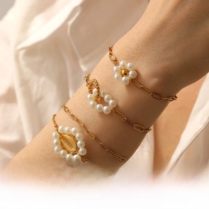 Dettaglio di bracciale dorato a strati con fiori di perle e ciondoli a conchiglia su polso
