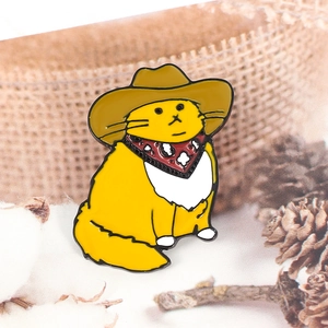 Close-up of yellow cowboy cat enamel pin with a brown hat and red paisley bandana