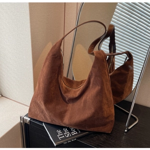 Detail of a brown suede hobo tote bag on a dark surface with soft window shadows