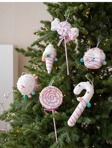 Pink and white knit candy ornaments hanging on a Christmas tree with soft warm lighting
