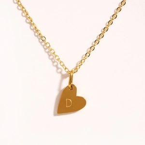 Détail d'un collier pendentif cœur doré avec une lettre majuscule D gravée dessus