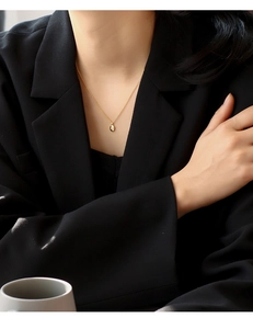 Detail shot of a minimalist gold starburst pendant necklace worn with a chic black blazer