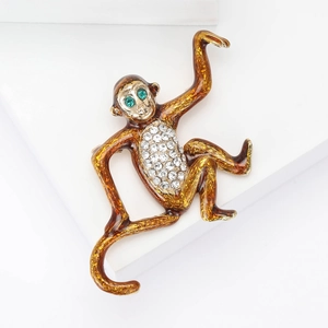 Detail of a gold monkey brooch with brown enamel body, white crystals and green eyes