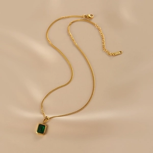 Elegant gold necklace with emerald green square pendant on soft beige silk fabric