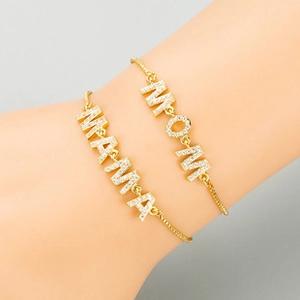 Detail of layered gold-plated bracelets featuring MAMA and MOM letter pendants with zircons