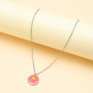 Close-up of a silver sunflower pendant with pink petals and yellow core on a beige stand