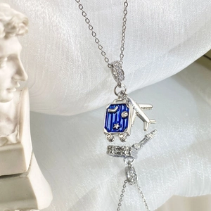 Detailed close-up of a blue enamel suitcase and silver airplane pendant on a chain